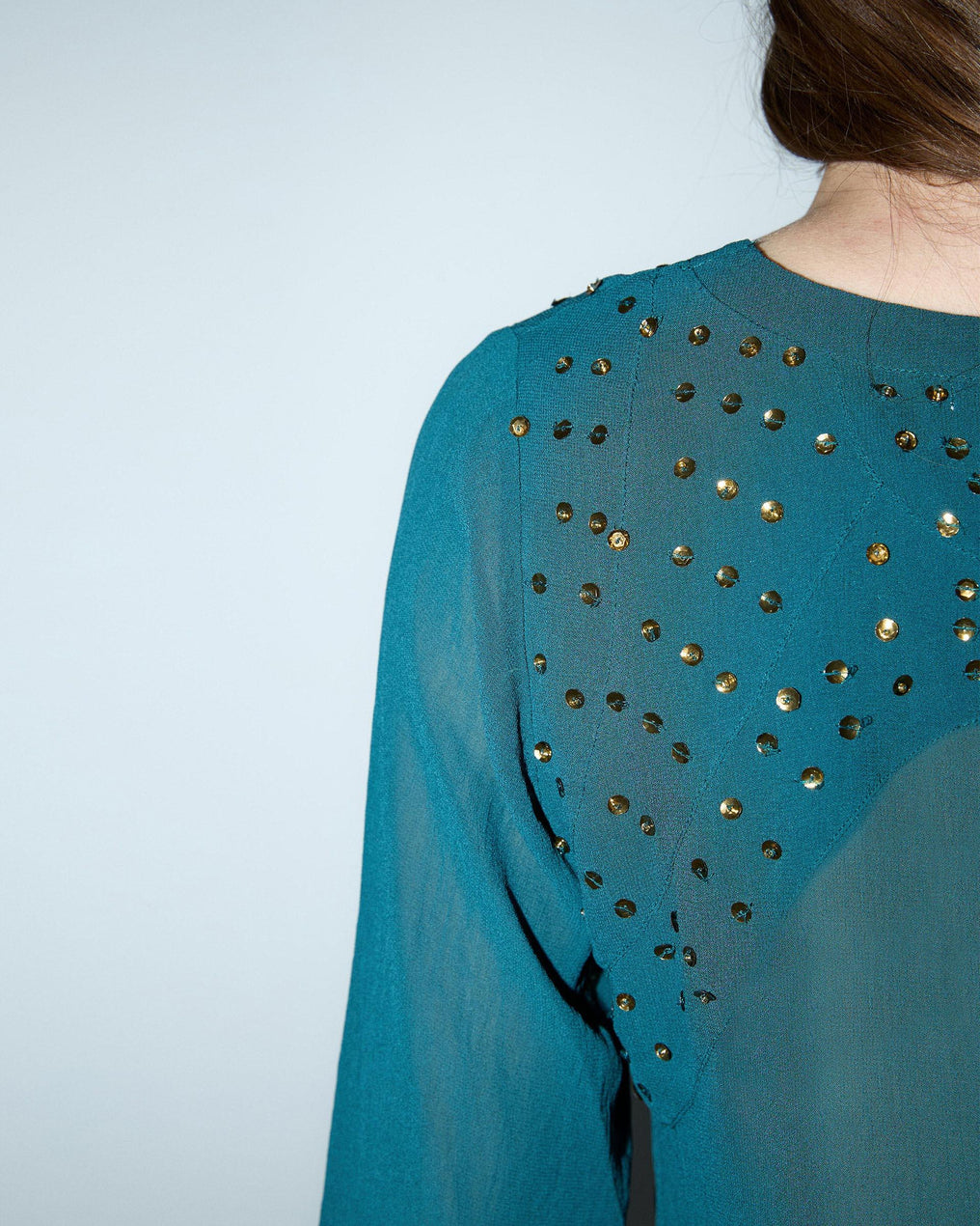 Blusa de lantejoulas, detalhe no decote em tom petróleo.