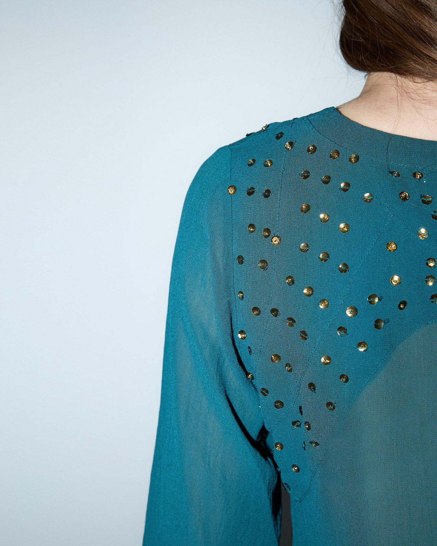 Blusa de lantejoulas, detalhe no decote em tom petróleo.